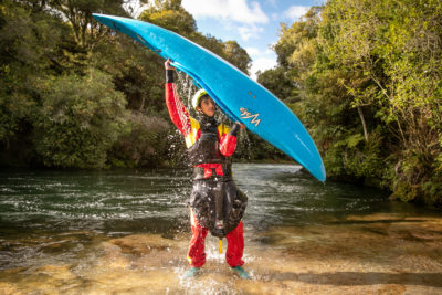 Paddler lifting kayak out of a river to check it for invasive weeds
